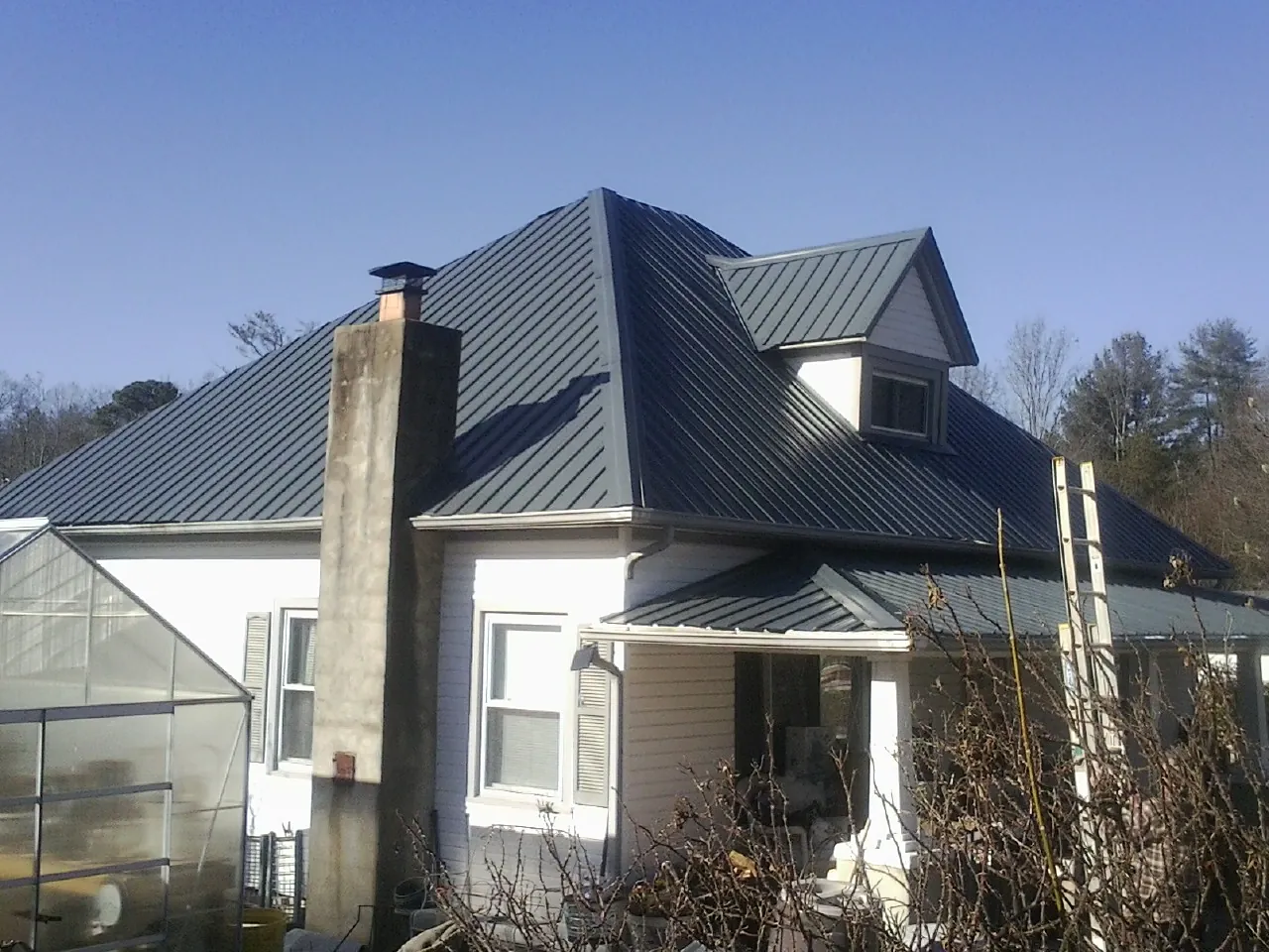 Dark blue standing seam metal roof on a white farmhouse with dormer — Slate & Tile Roof Repair by Roofing Brothers in Rumsey
