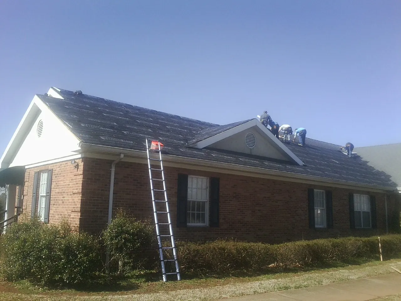 Crew tearing shingles off a brick ranch roof with a ladder set — Emergency Roof Repair work by our crew in Rumsey