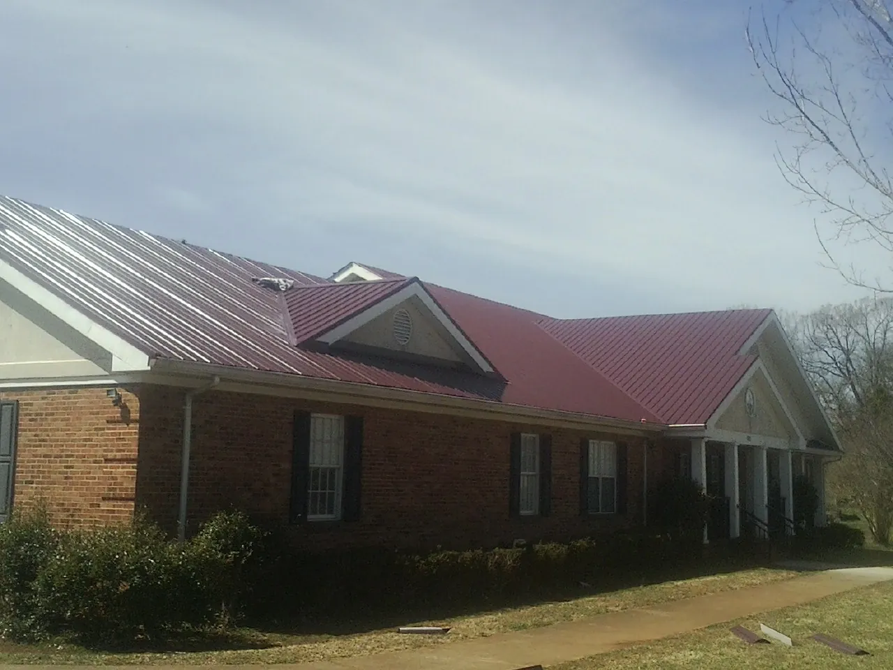 Red metal roof with gabled entries on a long brick building, from a Hail Damage Roof Repair job in Rumsey
