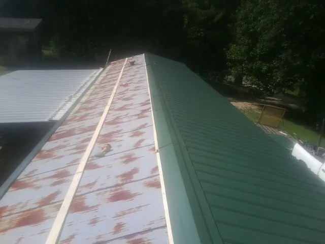 Old rusted panels beside newly installed green metal roofing — Wind Damage Roof Repair by Roofing Brothers in Rumsey