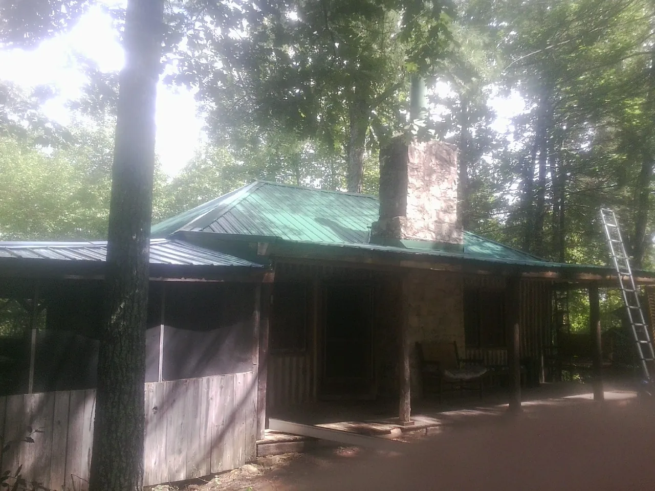 Green metal roof and stone chimney above a log cabin porch in Rumsey