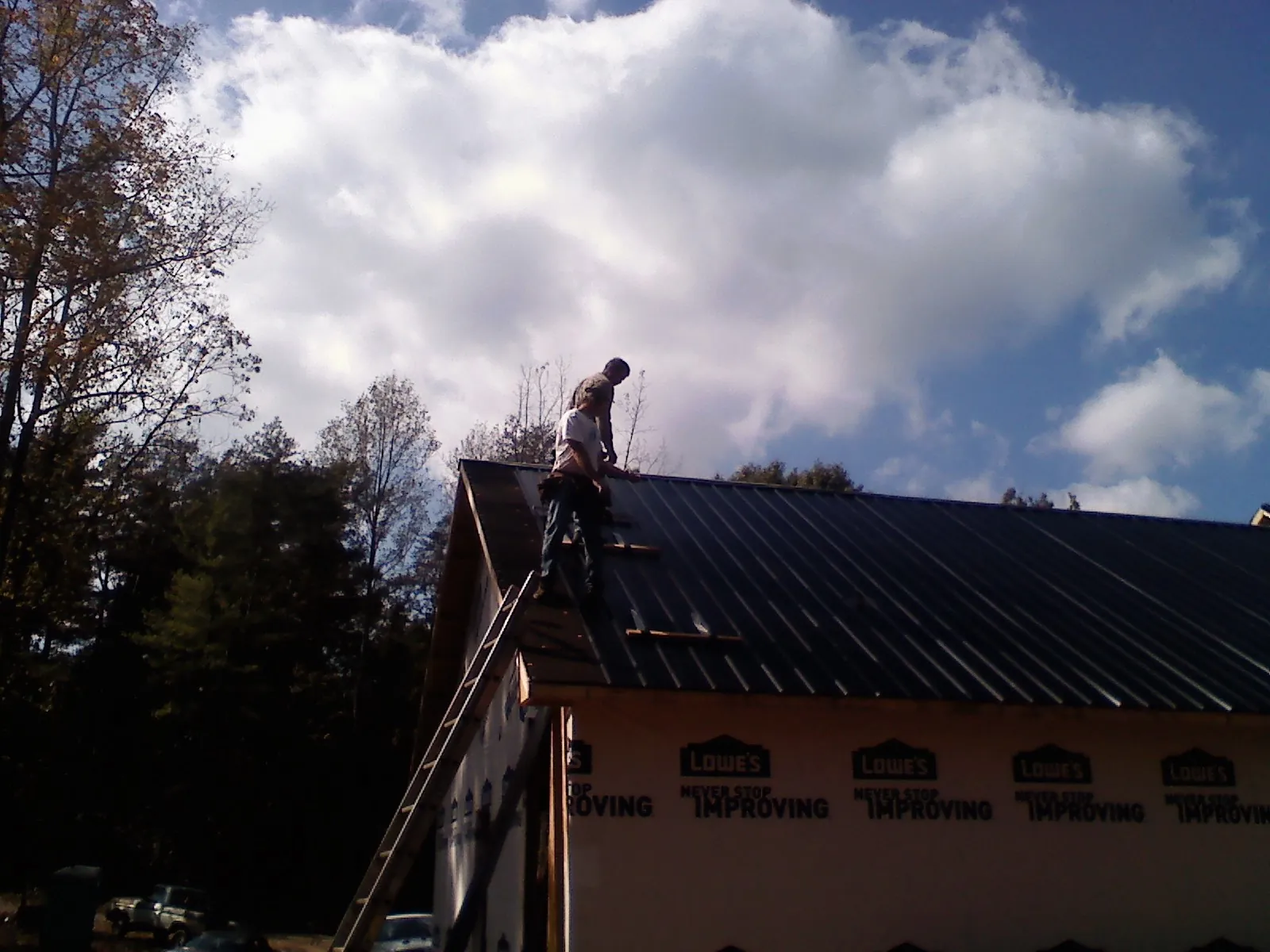 Roofer fastening dark metal panels high against a cloudy sky, from a Roof Inspection job in Rumsey