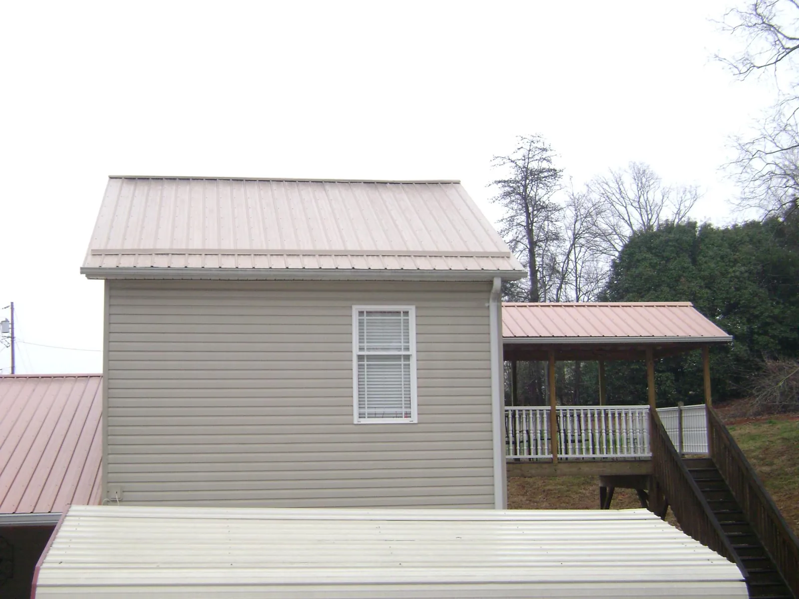 Tan metal roofs on a two story addition and attached porch, from a Roof Replacement job in Rumsey